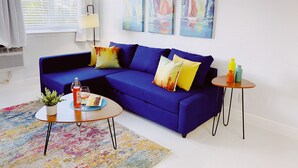 A modern living room with a blue sofa, colorful cushions, a small round table with drinks, a potted plant, and a colorful rug. - Spacious 2-Bed, 2-Bath in the Center of Miami w/ Free Parking (Miami)