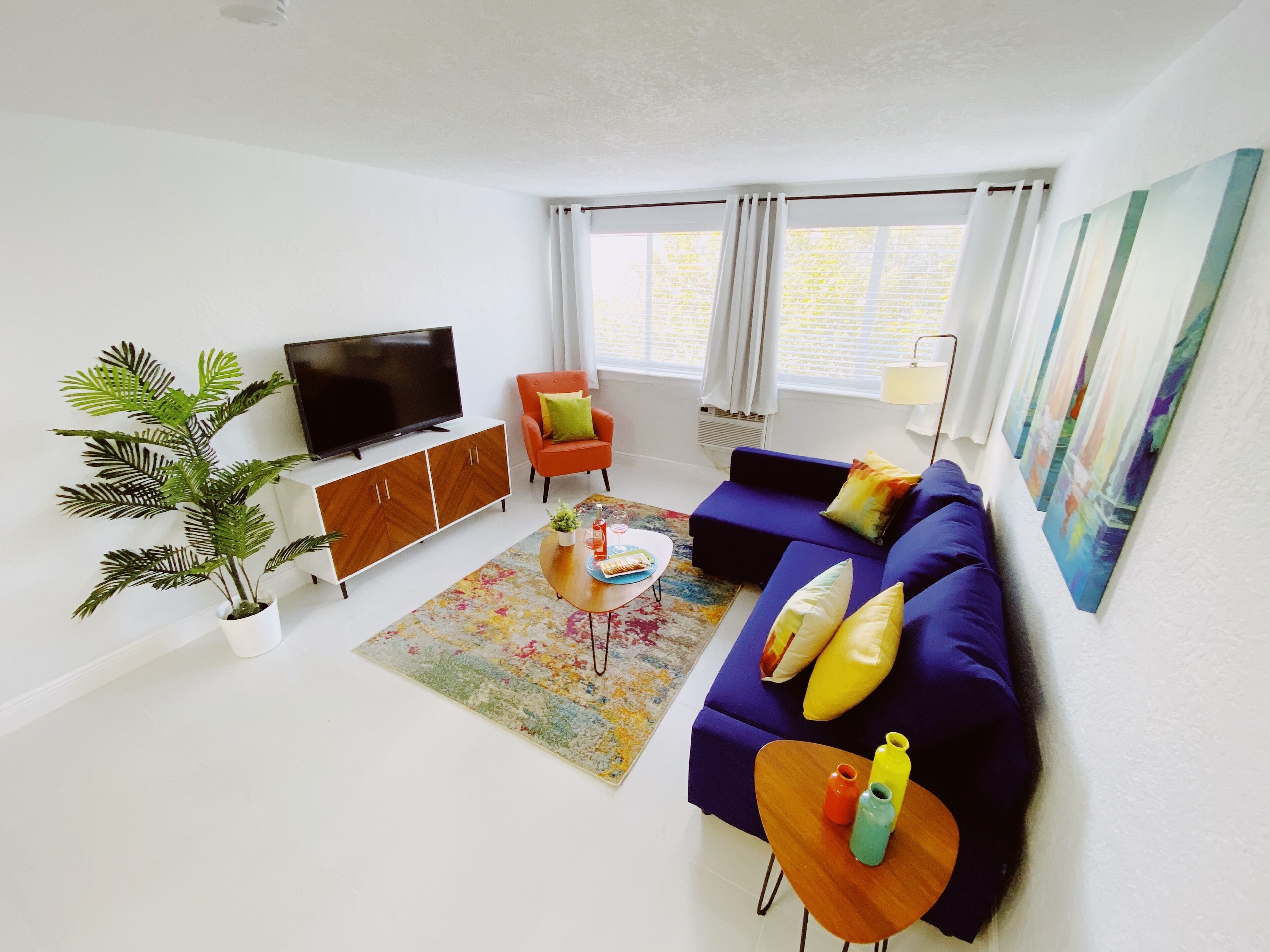 A modern living room with a sofa set, a television, a potted plant, and a colorful rug.