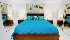 A modern bedroom with a large bed, two bedside tables with lamps, a mirror, and three wall-mounted paintings. - Spacious 2-Bed, 2-Bath in the Center of Miami w/ Free Parking (Miami)