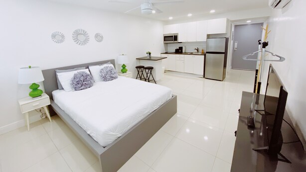 Une chambre moderne avec un lit, une table de chevet et, au fond, un petit coin cuisine.