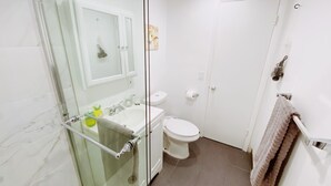 Une salle de bain avec une douche à parois de verre, un lavabo avec des articles de toilette, des toilettes et un porte-serviettes.