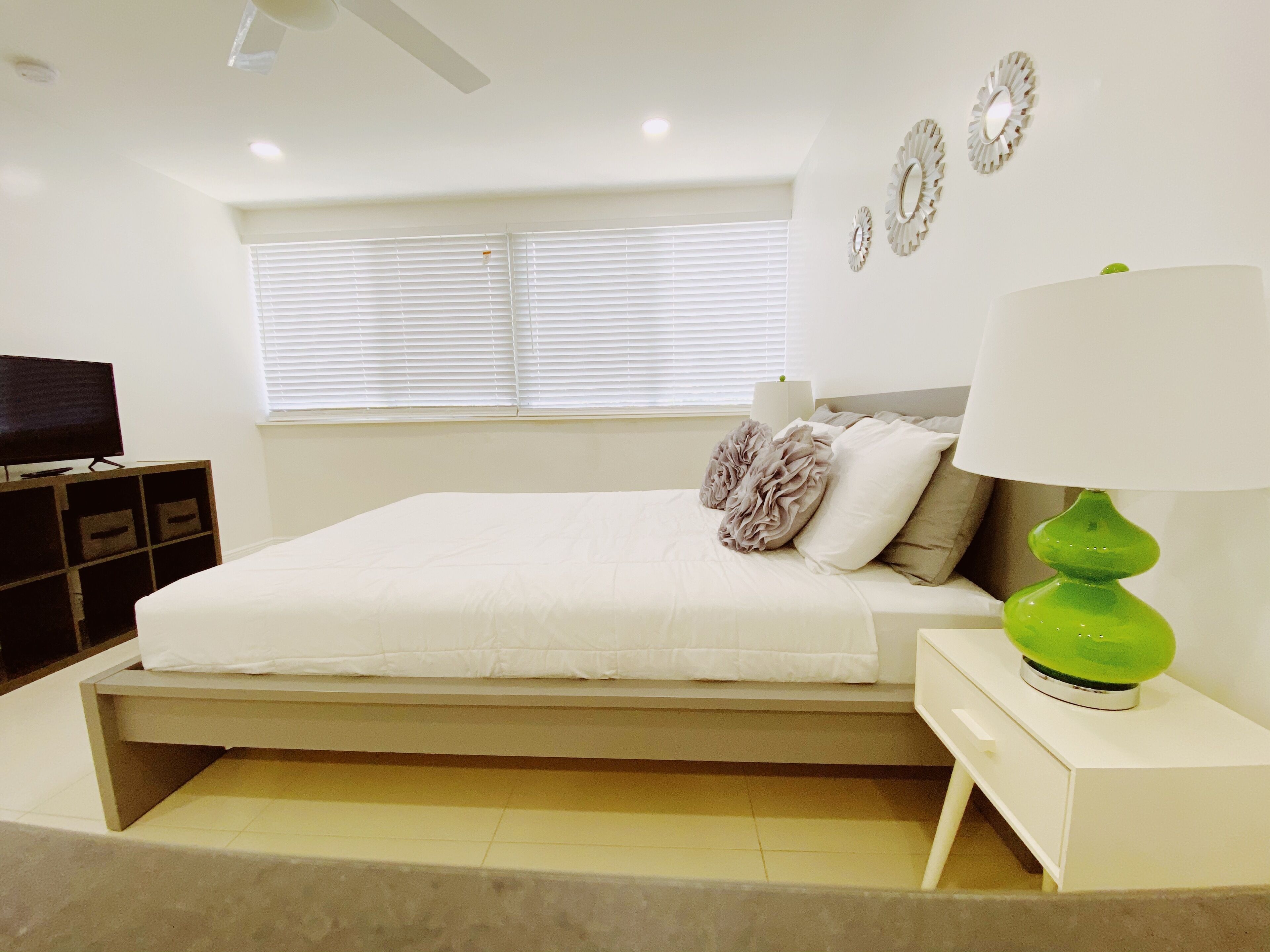A bedroom with a bed, a TV, a lamp, and a window with blinds.