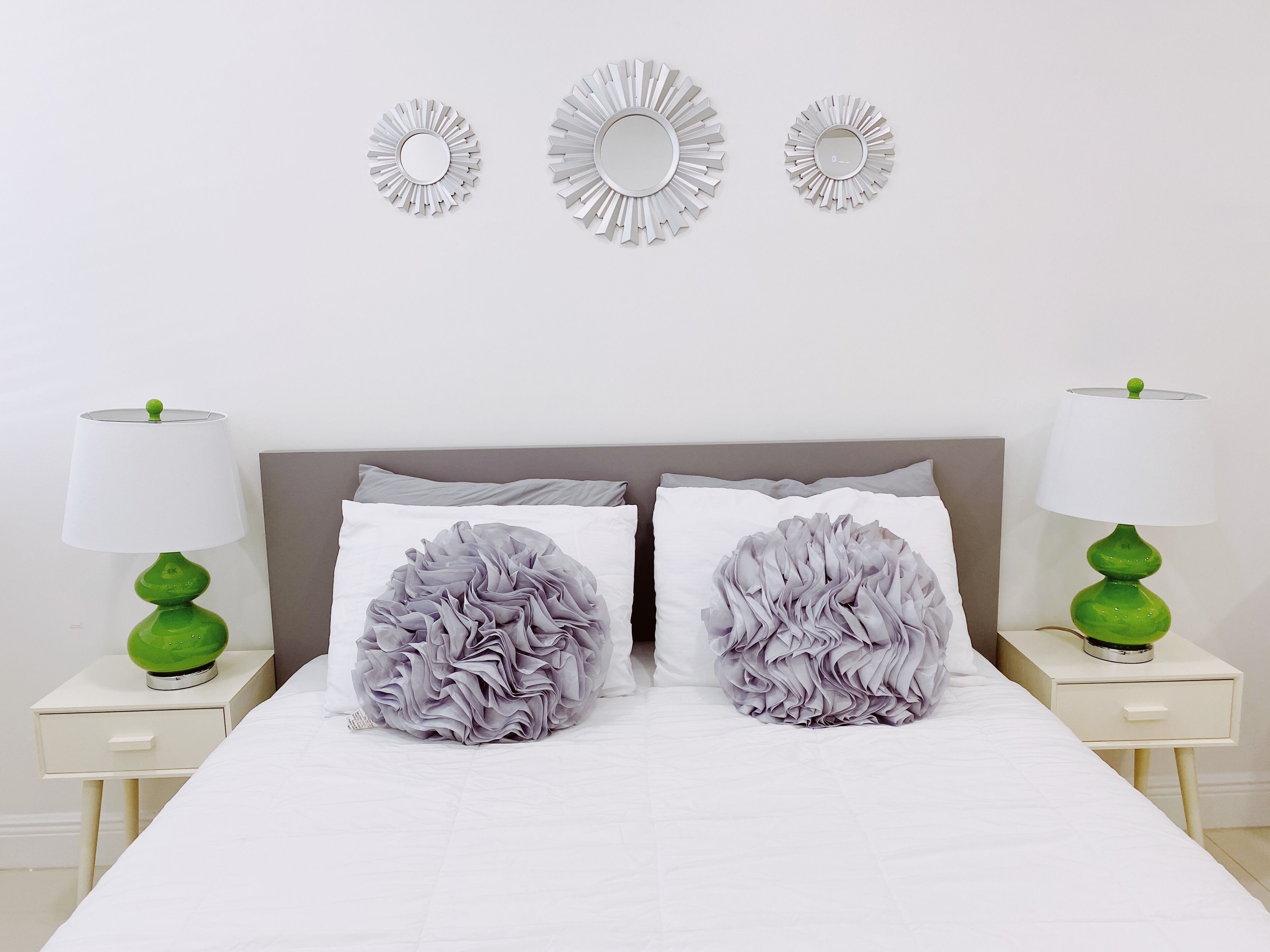 A bedroom with a bed, two nightstands, two lamps, and three wall mirrors.