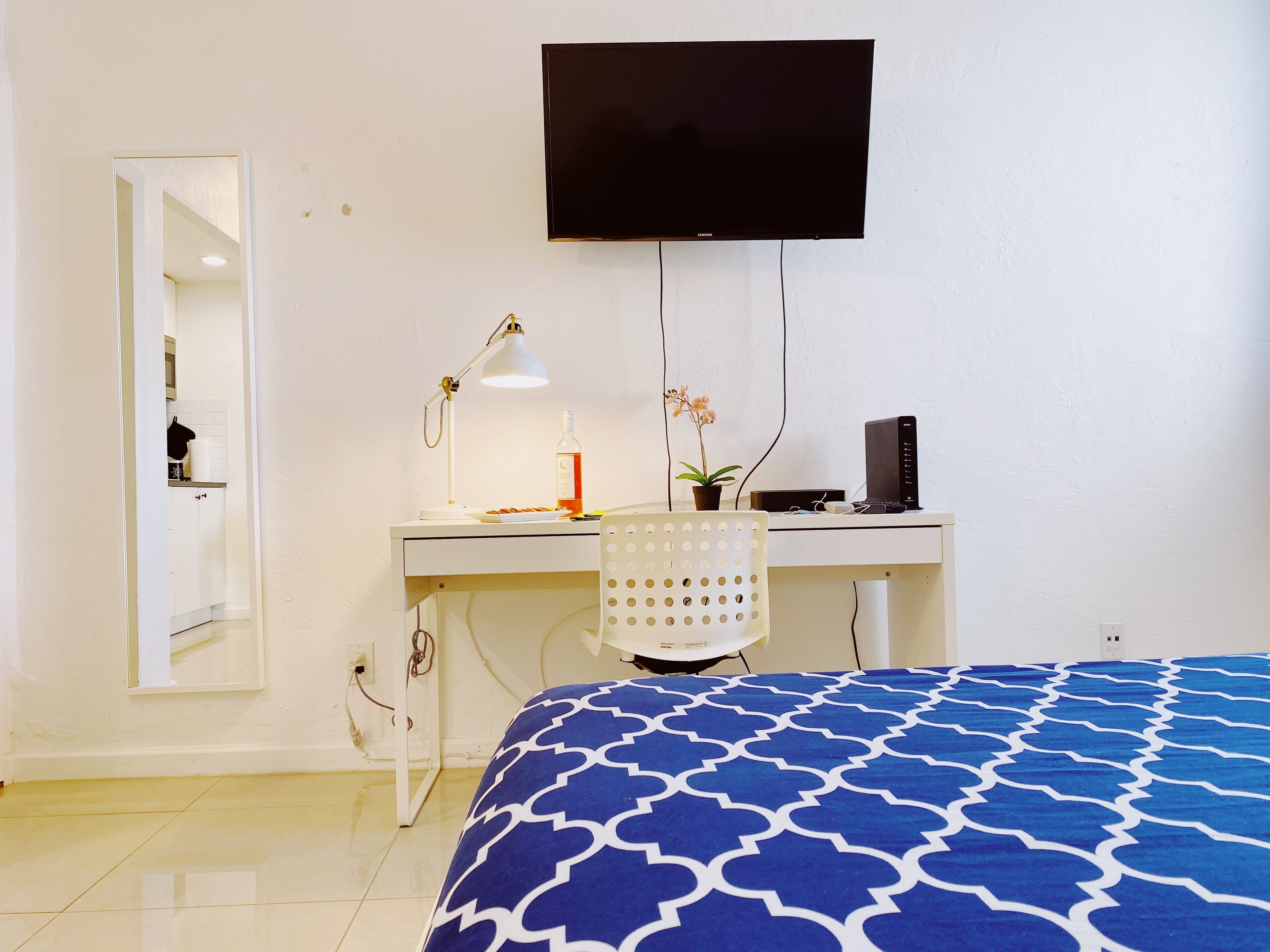 Ein Hotelzimmer mit einem Bett, einem Schreibtisch mit Computer, einem Fernseher, einer Lampe und einer Zimmerpflanze.