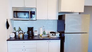A modern kitchen with white cabinets, a stainless steel refrigerator, a microwave, a coffee maker, and a toaster. - Central Miami Studio w/ Parking - Coconut Grove (Miami)