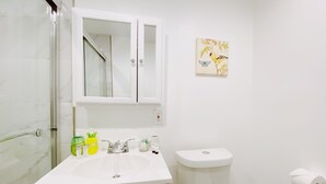A bathroom with a white sink, mirror, and toilet. There are toiletries on the sink and a painting on the wall. - Central Miami Studio w/ Parking - Coconut Grove (Miami)