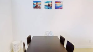 Ein Essbereich mit einem langen Tisch, sechs Stühlen und drei an der Wand befestigten Bildern mit Küstenmotiven.