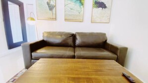 Ein Wohnzimmer mit einem braunen Ledersofa, einem Holztisch und drei abstrakten Bildern an der Wand.