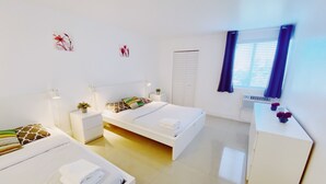 A modern hotel room with two beds, a desk, and a window with blinds. - Comfy 1-Bedroom Apartment w/ parking - Coconut Grove (Miami)