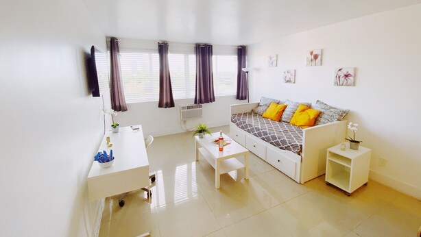 A bright, modern living room with a white sofa, a small white table, and a white cabinet. - Comfy 1-Bedroom Apartment w/ parking - Coconut Grove (Miami)