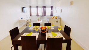A dining area with a table set for four, a TV mounted on the wall, and a window with curtains. - Comfy 1-Bedroom Apartment w/ parking - Coconut Grove (Miami)