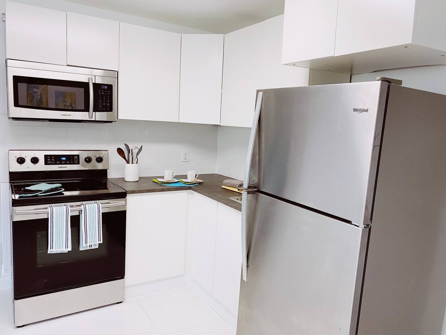 A modern kitchen with white cabinets, a stainless steel refrigerator, a microwave, and an oven.