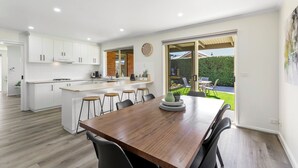 A modern kitchen with white cabinets, a central island, and a dining area with a wooden table and bar stools. - 2 Bedroom - Walk to Beach - Pet Friendly (Ocean Grove)