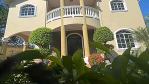 A two-story house with a balcony, columns, and a symmetrical facade. - Casa Familiar , donde disfrutarás de un relajante alojamiento. (Tela)