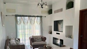 A spacious living room with a large sofa, a smaller sofa, and a coffee table. There is a TV mounted on the wall and a chandelier hanging from the ceiling. - Casa Familiar , donde disfrutarás de un relajante alojamiento. (Tela)