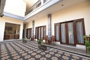 A spacious indoor area with a patterned floor, wooden furniture, and large windows with curtains. - Samudra Homestay (Kuta)