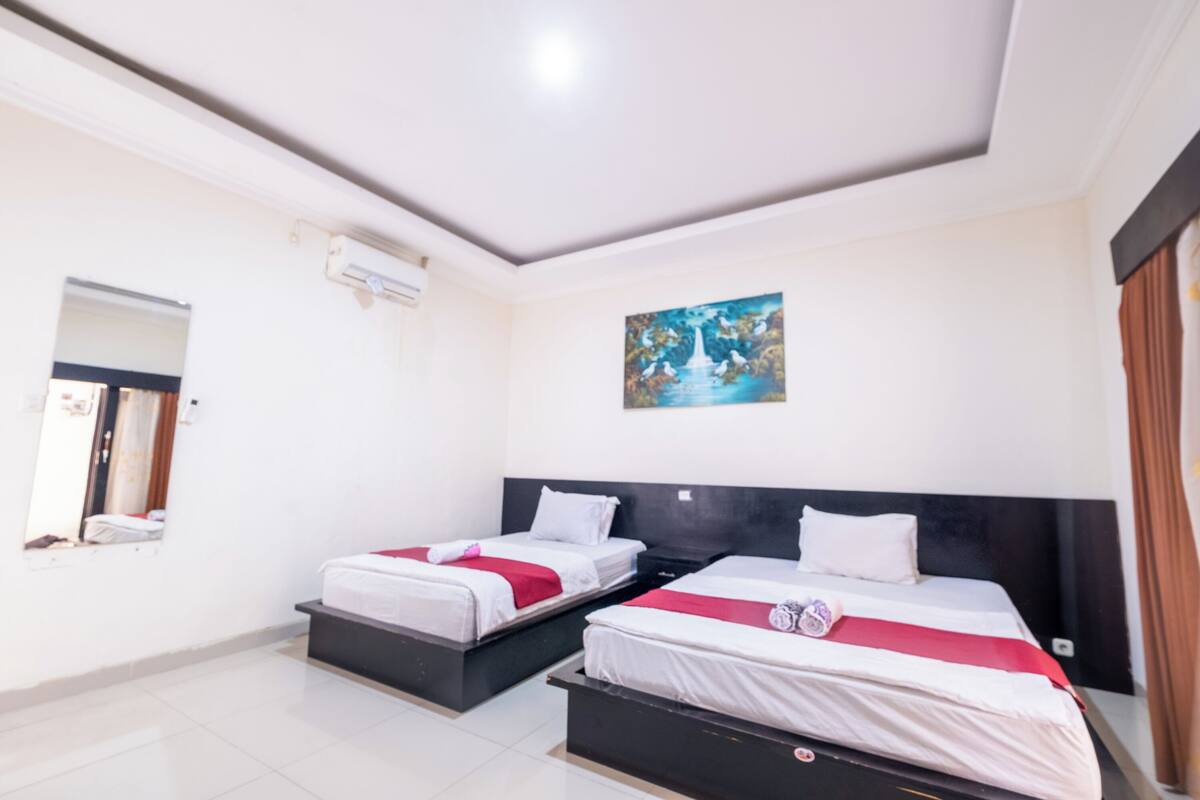 A hotel room with two beds, a large mirror, a painting on the wall, and a window with curtains.