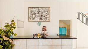 A reception desk with a clock, framed artwork, and a plant. - Samudra Homestay (Kuta)