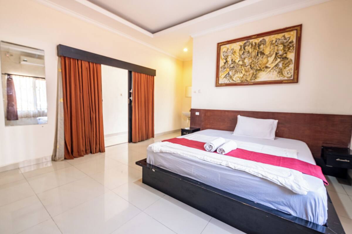 A hotel room with a large bed, a painting on the wall, and a door with curtains.