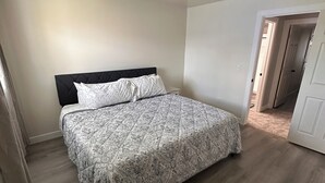 Un dormitorio con cama, cabecera, luz en el techo y una puerta que da a otra habitación.