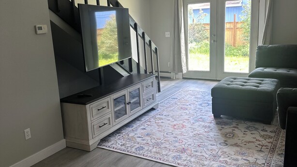 Una sala de estar con una escalera moderna, un televisor de pantalla plana, un sofá verde y un tapete estampado.