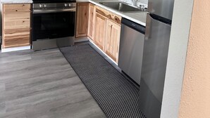 Una cocina moderna con armarios de madera, electrodomésticos de acero inoxidable y un tapete con estampado blanco y negro.