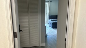 Un pasillo con un armario blanco cerrado, un sofá gris al fondo y un suelo de madera gris.