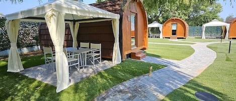 Un jardín con zona de estar techada, un sendero de ladrillo y construcciones de madera.