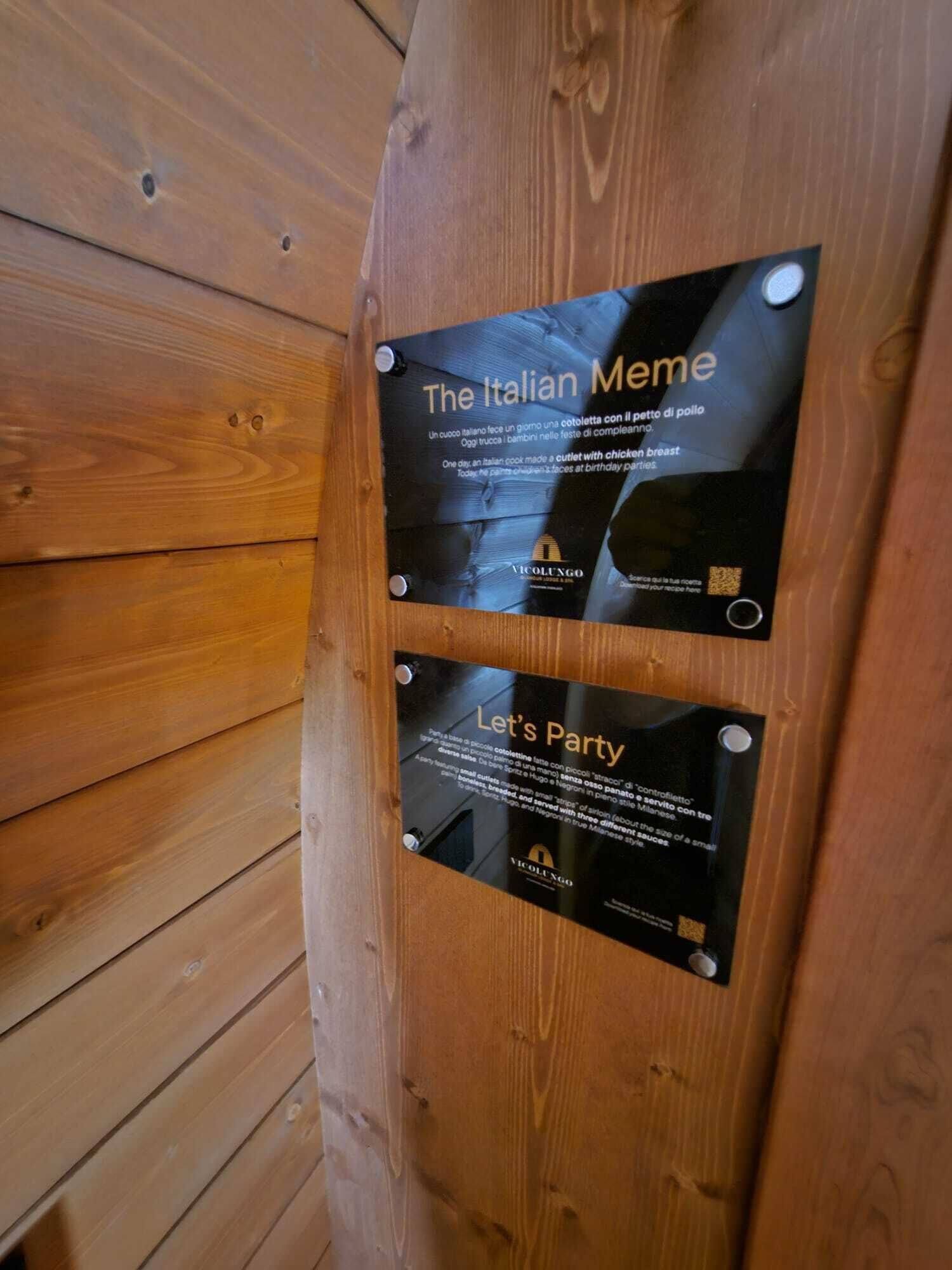A wooden wall with two black plaques. One plaque reads "The Italian Meme" and the other "Let's Party".