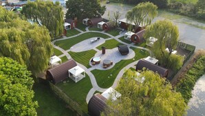 A campsite with multiple wooden cabins, a central gathering area with a barbecue, and a river nearby. - VICOLUNGO Glamor Lodge & Spa Ondaland waterpark (Vicolungo)