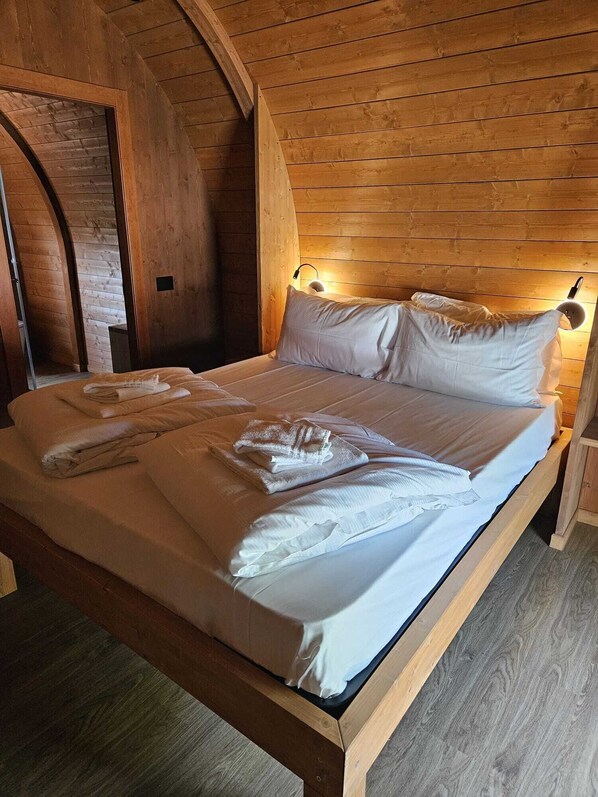 A wooden bed with white linens and towels, in a room with wooden walls and a sloped ceiling. - VICOLUNGO Glamor Lodge & Spa Ondaland waterpark (Vicolungo)