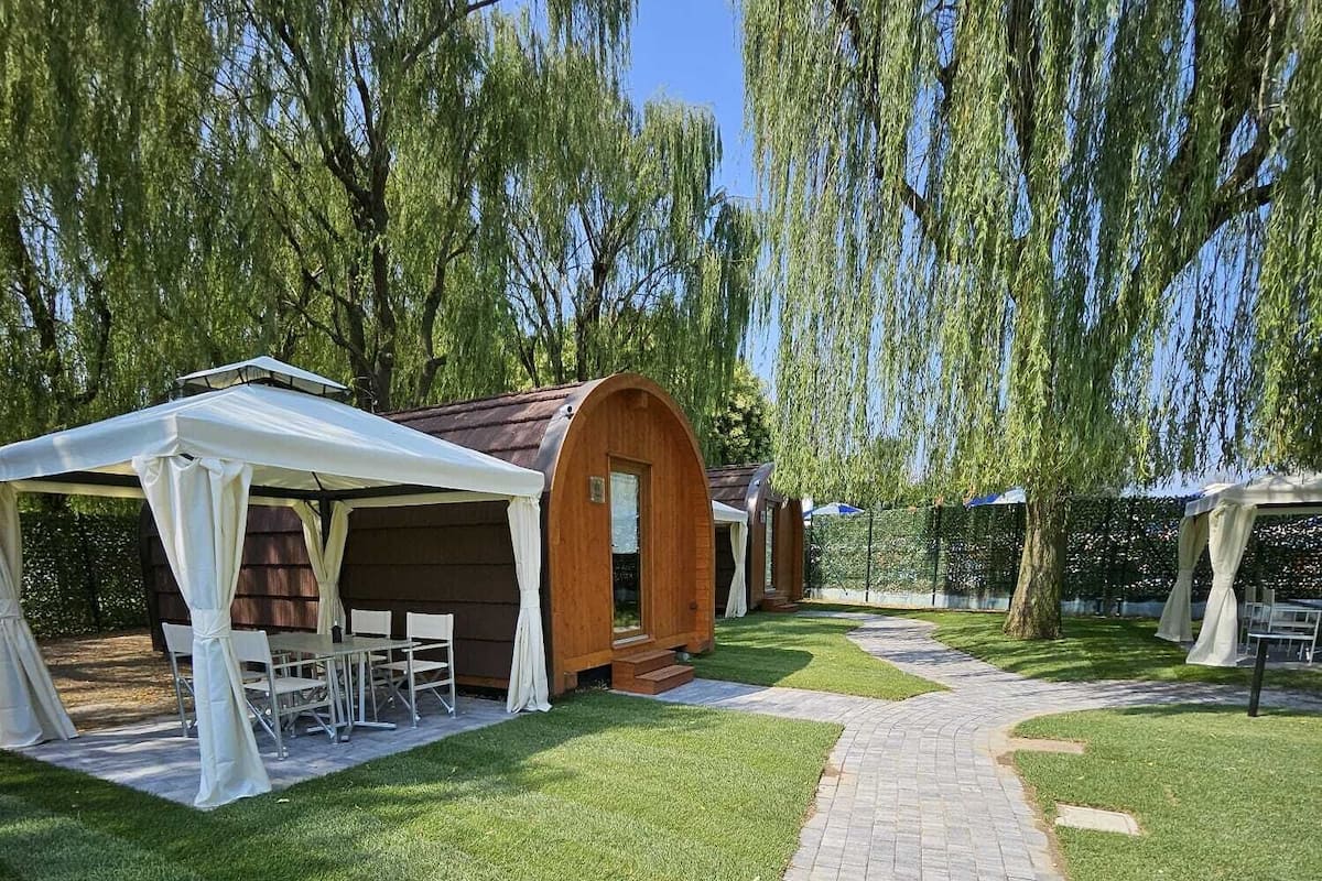 A pathway leading to a row of wooden cabins with white canopies, surrounded by lush greenery and trees.