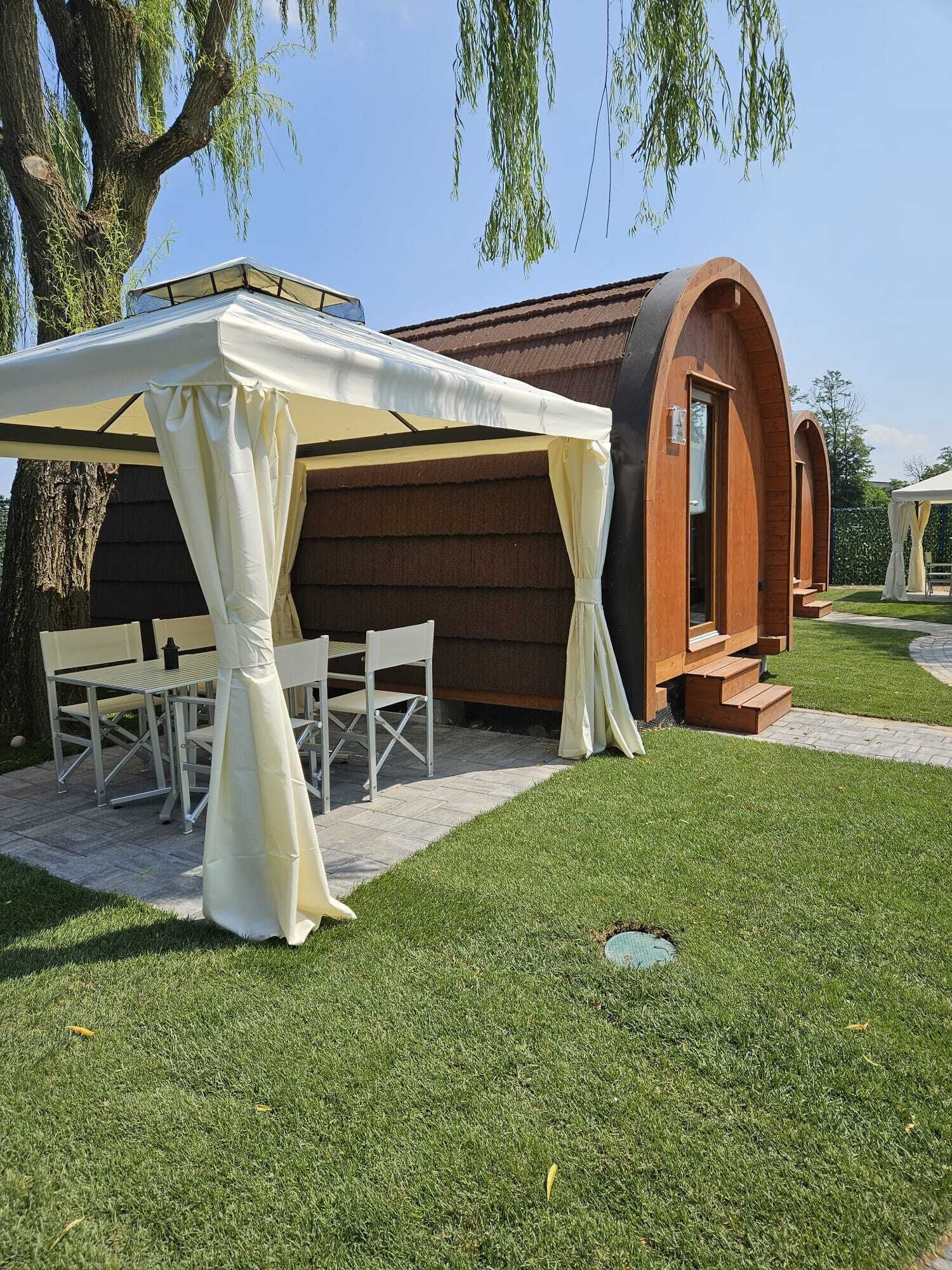 Un espacio al aire libre cubierto con mesa y sillas, una estructura de madera con entrada arqueada y un césped bien cuidado.