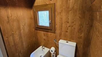 A small, wooden bathroom with a window, a bidet, and a toilet.