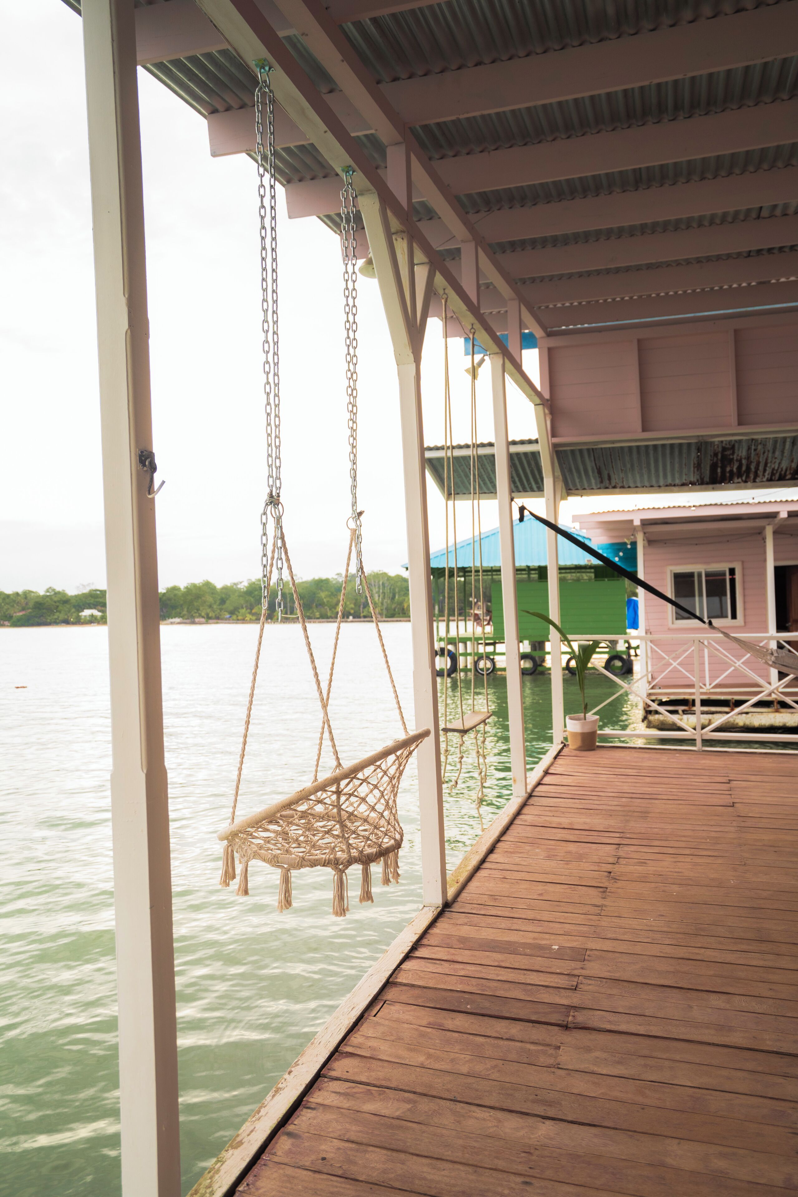 A wooden deck with a swing chair and a hanging swing, overlooking a body of water.