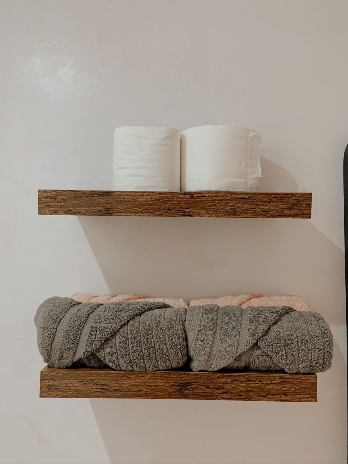 Two wooden shelves with rolled towels, one white and one gray.
