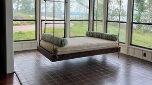 Amplia habitación con ventanas grandes, una hamaca colgante y un ventilador de techo.