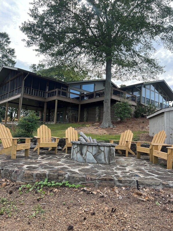 A cabin with a stone fire pit and wooden Adirondack chairs.