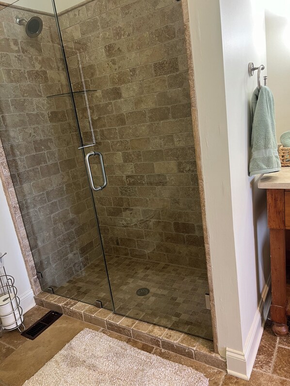 A shower with a glass door and a metal handle, a towel hanging on a rack, and a small shelf with a basket.