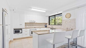 A modern kitchen with white cabinets, a built-in microwave, a large island with bar stools, and a window with a view of greenery.
