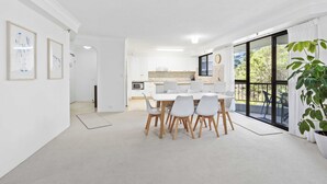 A modern, well-lit room with a dining table and chairs, a kitchen area, and a large sliding glass door leading to an outdoor balcony.