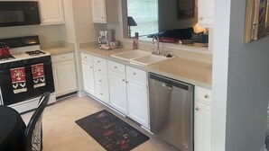 Una cocina moderna con armarios blancos, un lavavajillas de acero inoxidable y una cafetera.