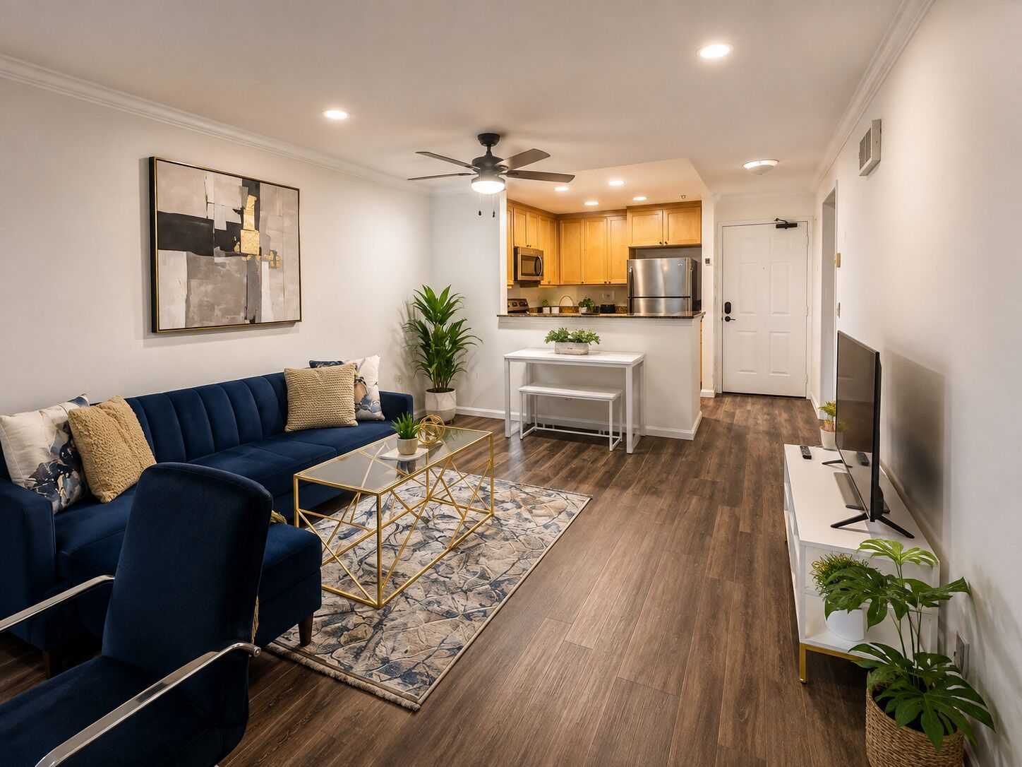 A modern living room with a blue sofa, a glass coffee table, and a kitchen in the background.