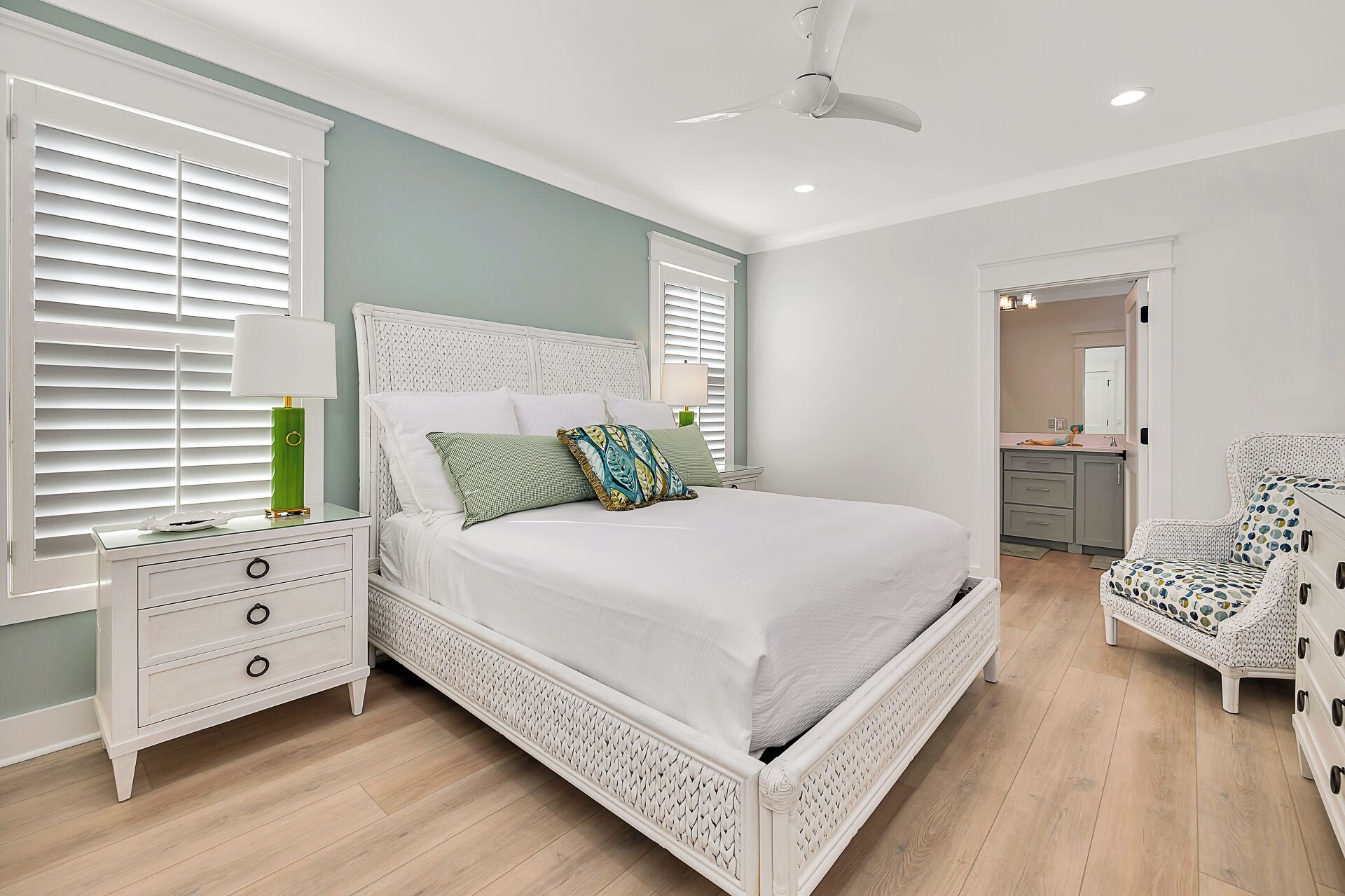 A bedroom with a white bed, a nightstand, a chair, and a ceiling fan.