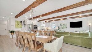 A modern kitchen with wooden beams, a dining area with a wooden table and chairs, and a green sofa in the living area.