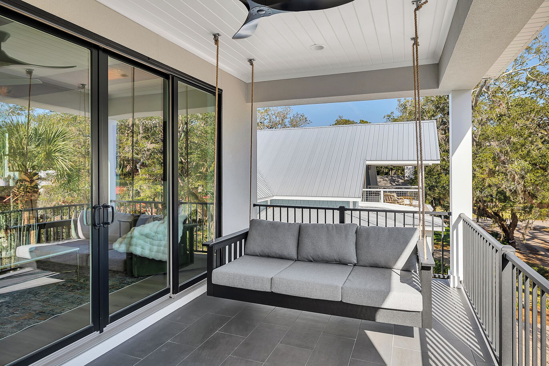 Un balcon moderne avec une porte vitrée, un banc rembourré et une vue sur une maison et des arbres.