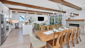 A modern kitchen with white cabinetry, a large island, and a dining area with wooden chairs and a table.