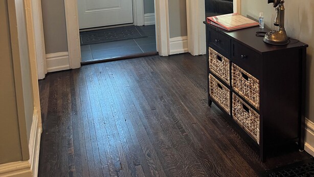 Un pasillo con piso de madera oscura, una puerta con ventanal esmerilado y una consola de madera oscura con cestas.