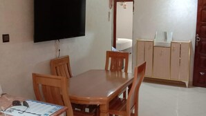 Een eetgedeelte met een houten tafel en stoelen, een flatscreen televisie aan de muur en een keuken zichtbaar door een boogvormige doorgang.
