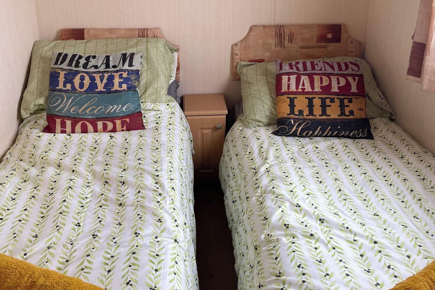Two single beds with floral-patterned bedding and decorative pillows with inspirational phrases.